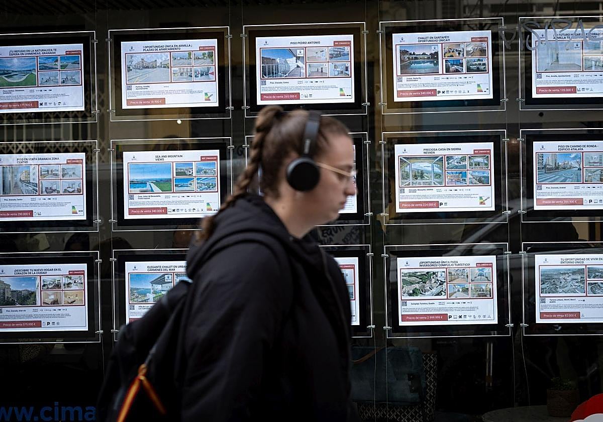 Una joven pasa por el escaparate de una inmobiliaria.