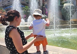 Una mujer sostiene a su bebé frente a la fuente de la plaza de la Constitución.