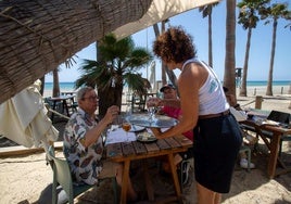 Una camarera sirve a unos clientes en el chiringuito Awa de Playa Granada, que este año ha renovado su plantilla.