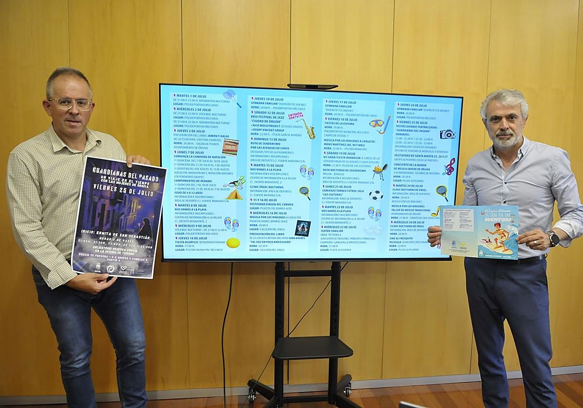 De izquierda a derecha el primer teniente de alcalde del Ayuntamiento de Órgiva, José Miguel Herrera, y el alcalde de Órgiva, Raúl Orellana mostrando en una pantalla de televisión la programación cultural del mes de julio