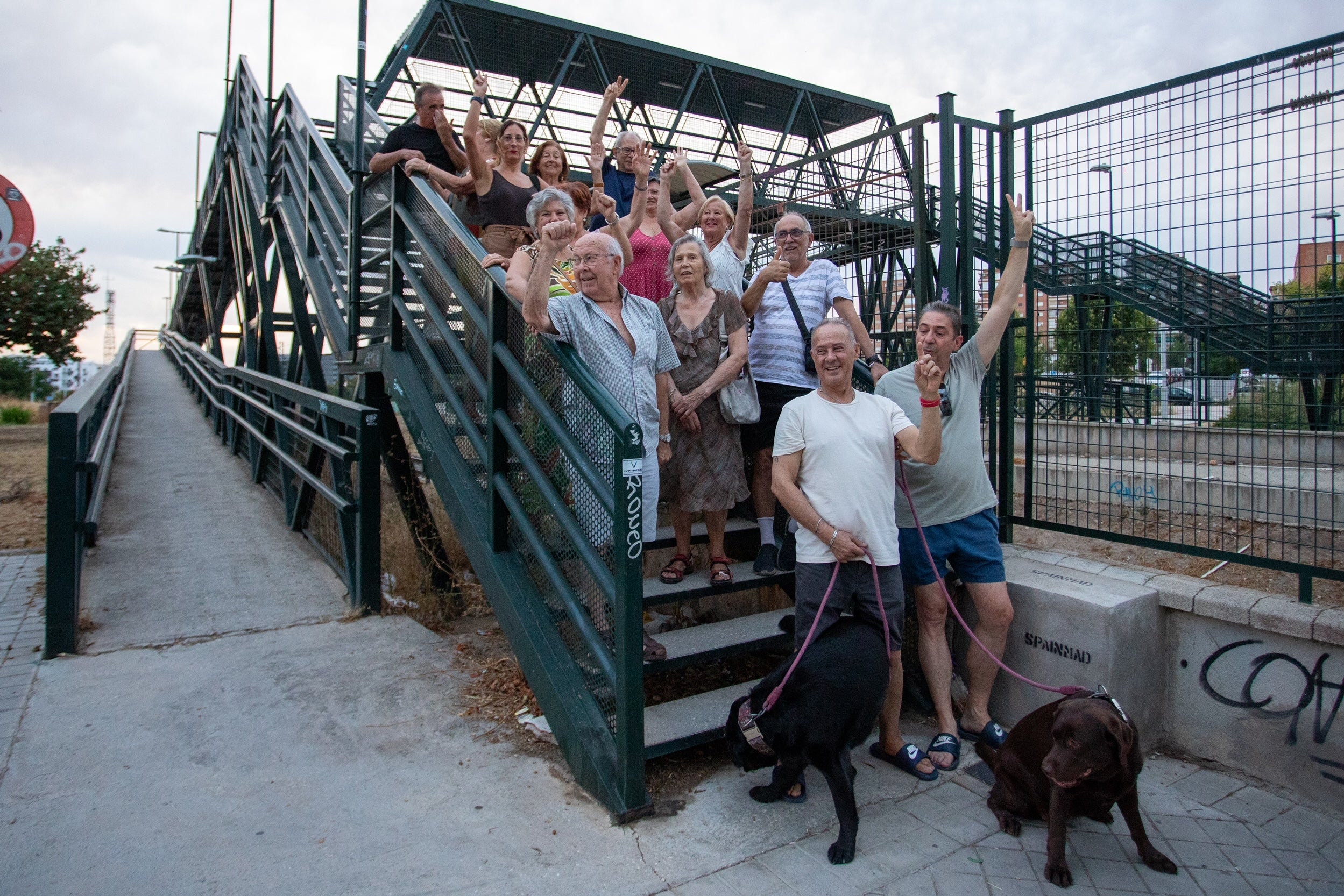 Un grupo de vecinos saluda desde la pasarela que salva las vías del tren nunca soterradas entre su barrio y La Chana