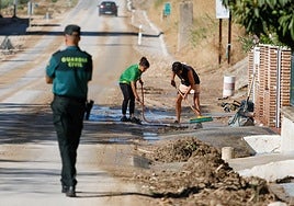 Vecinos de Zujaira limpian la entrada de sus casas. Un guardia civil controla el tráfico en la carretera, donde los restos del barro son evidentes.