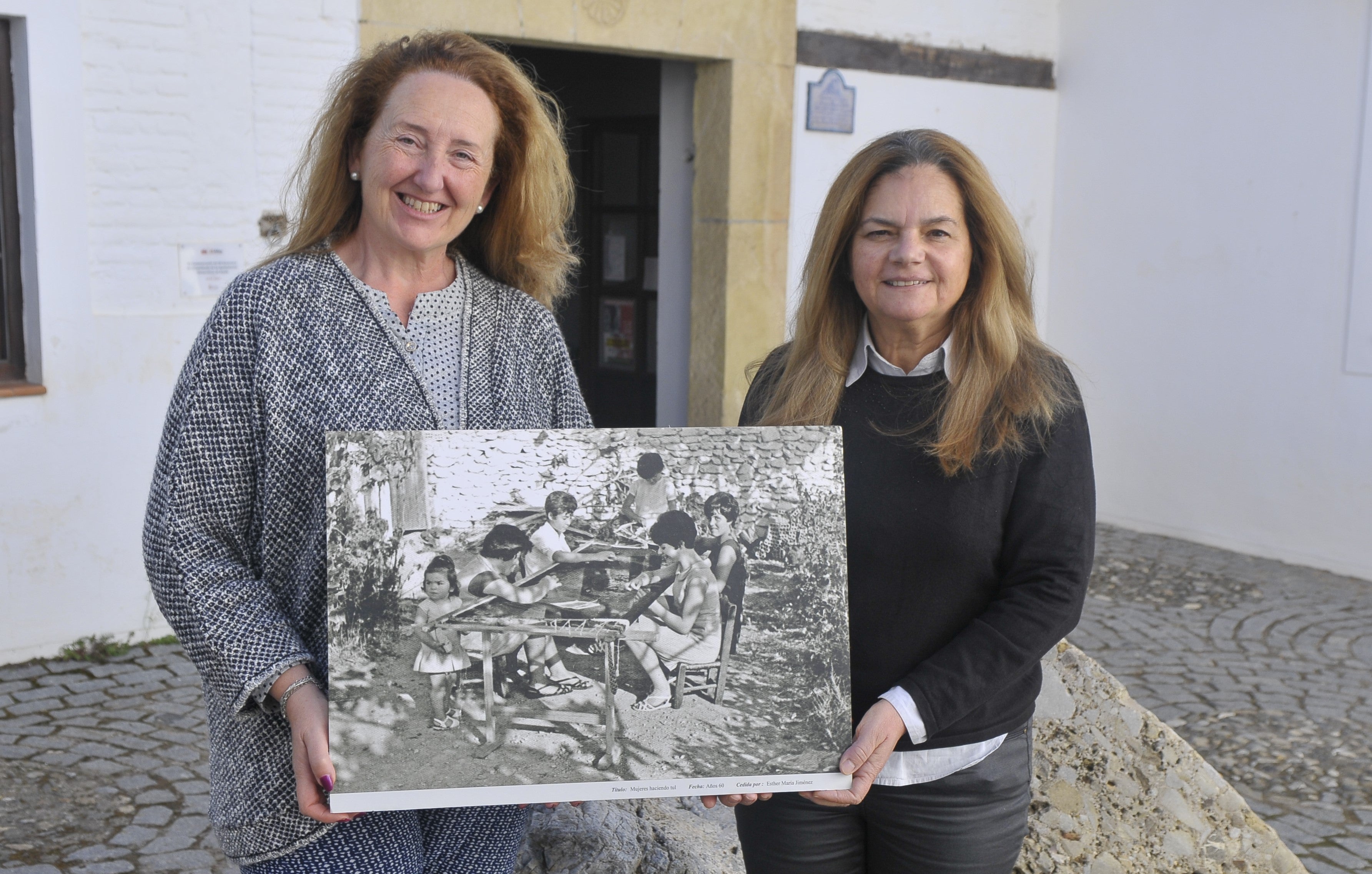 La concejala del Ayuntamiento de Nigüelas, Mari Carmen Alarcón (izquierda) y la primer teniente de alcalde María Lina Ortega, muestran una foto antigua de unas bordadoras de tul de su pueblo