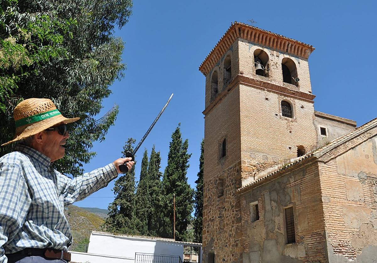 Un vecino del pueblo de Yátor señala el campanario de la torre de la iglesia de Yátor.