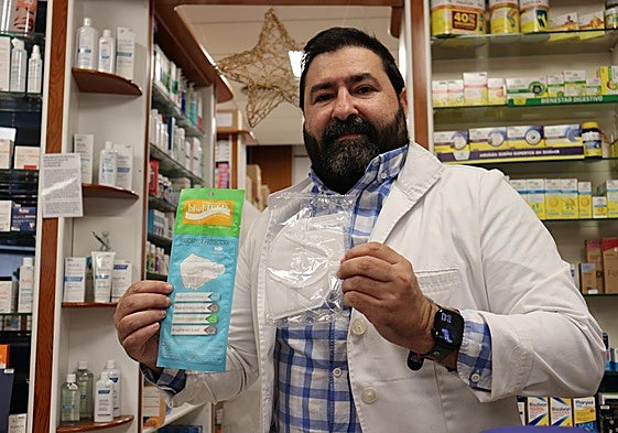 José Luis muestra dos modelos de mascarillas que vende en su farmacia.