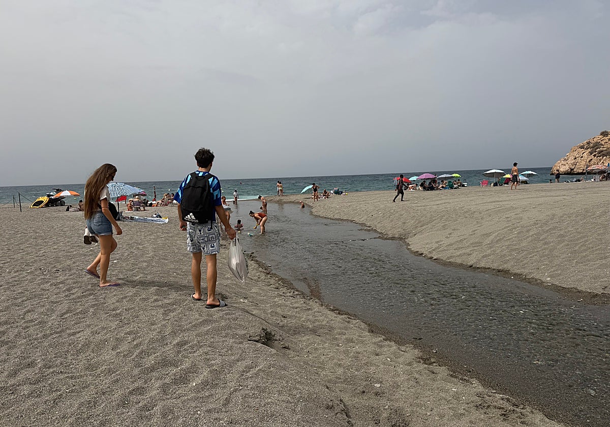 Unos bañistas en la playa de Salobreña junto a un balate por el que sale agua.