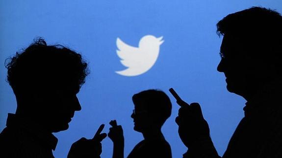 Varias personas consultan su móvil bajo el logotipo de Twitter 
