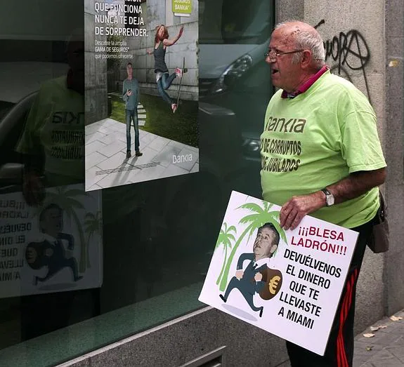 Un hombre pasa junto a una sucursal de Bankia con un cartel de protesta. 