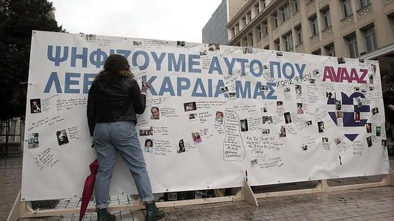 Una mujer escribe en un cartel en Atenas con el título: 'Votamos con el corazón'.
