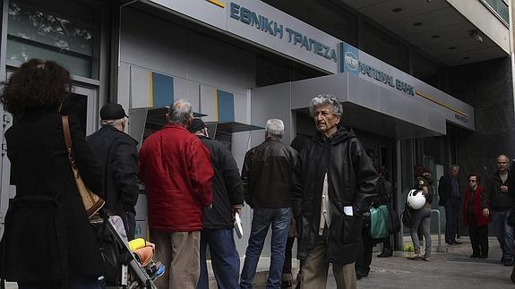Varias personas hacen cola en un cajero automático situado a la entrada de una sucursal del Banco Nacional Griego en Atenas. 