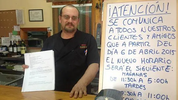 Manuel muestra sus papeles junto a un cartel que indica que habrá cambio de horario en el bar.