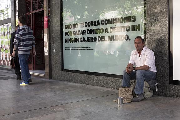 Un hombre maduro que dice estar sin recursos y con familia pide dinero en la Gran Vía ante el escaparate de un banco que ofrece sus productos.