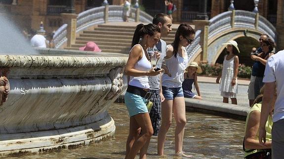 Turistas se refrescan en la fuente en la Plaza de España de Sevilla para mitigar los efectos del calor.