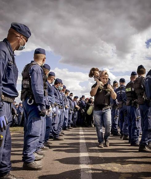 Un cordón de la Policía húngara vigila el avance de un padre y su hija hacia un autobús, en Roszke. :: 