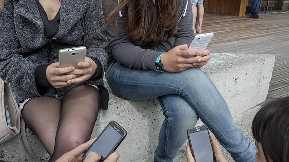 Varios jóvenes volcados en chatear con el móvil renuncian a conversar entre ellos, una escena habitual hoy en día. 