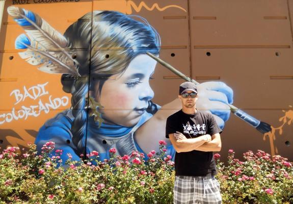 El artista granadino Badi posa ante su grafiti que acaba de terminar de pintar en la Carretera de Jaén. 