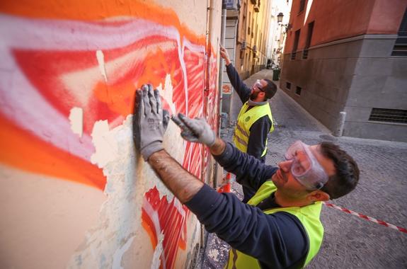 Dos operarios, rasqueta en mano, se emplean a fondo contra las pintadas. 