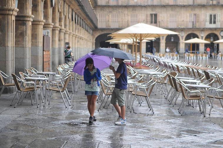 Dos personas con paraguas en la Plaza Mayor.