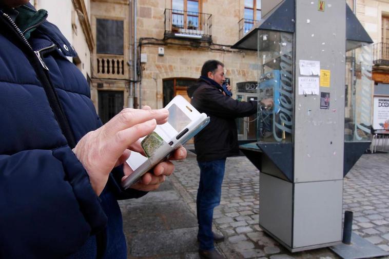 Un usuario utiliza su teléfono móvil junto a una cabina ubicada en la isleta de la calle la Rúa.