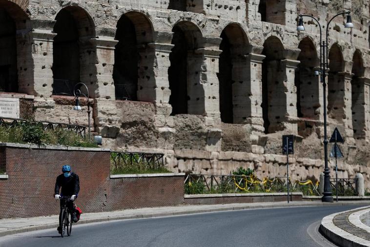 Un hombre con mascarilla monta en bicicleta cerca del Coliseo romano.