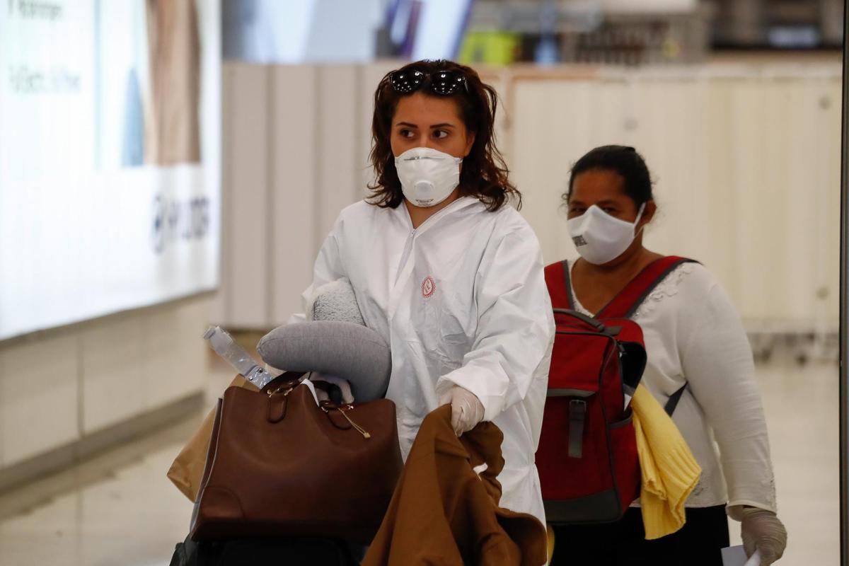 Una mujer protegida con mascarilla y traje EPI pasa los controles en la terminal 4 de Madrid-.