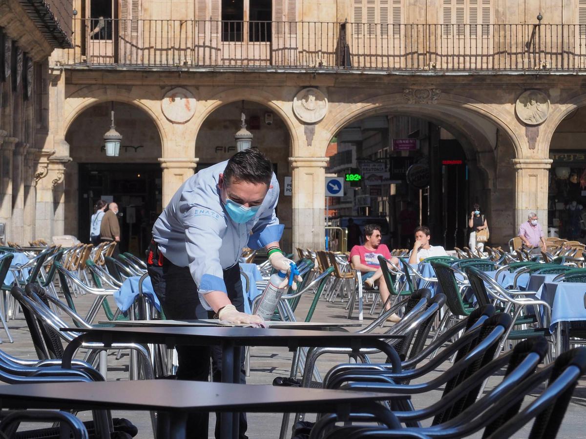 Un camarero limpia una mesa en la Plaza Mayor con la mascarilla puesta.