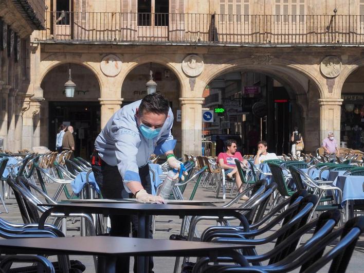 Un camarero limpia una mesa en la Plaza Mayor con la mascarilla puesta.