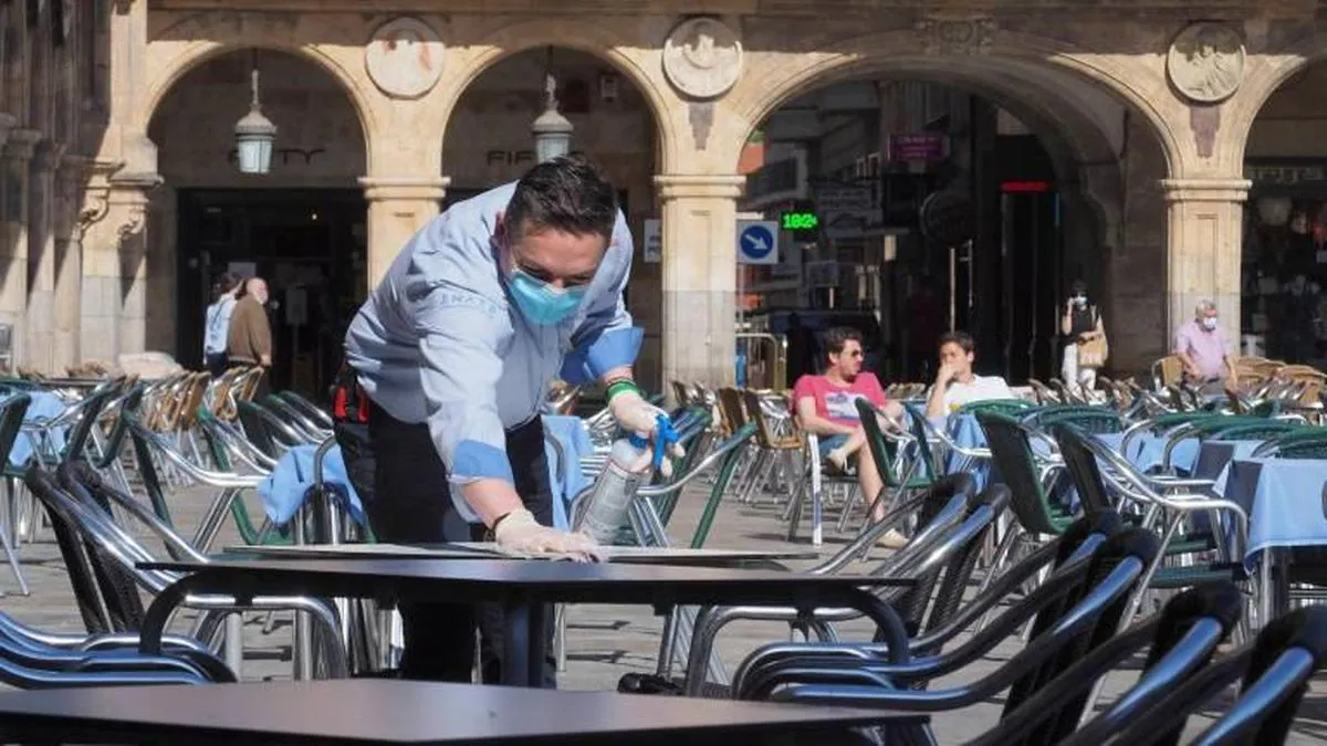 Un camarero limpiando y desinfectando una mesa tras su uso en una terraza en la Plaza.