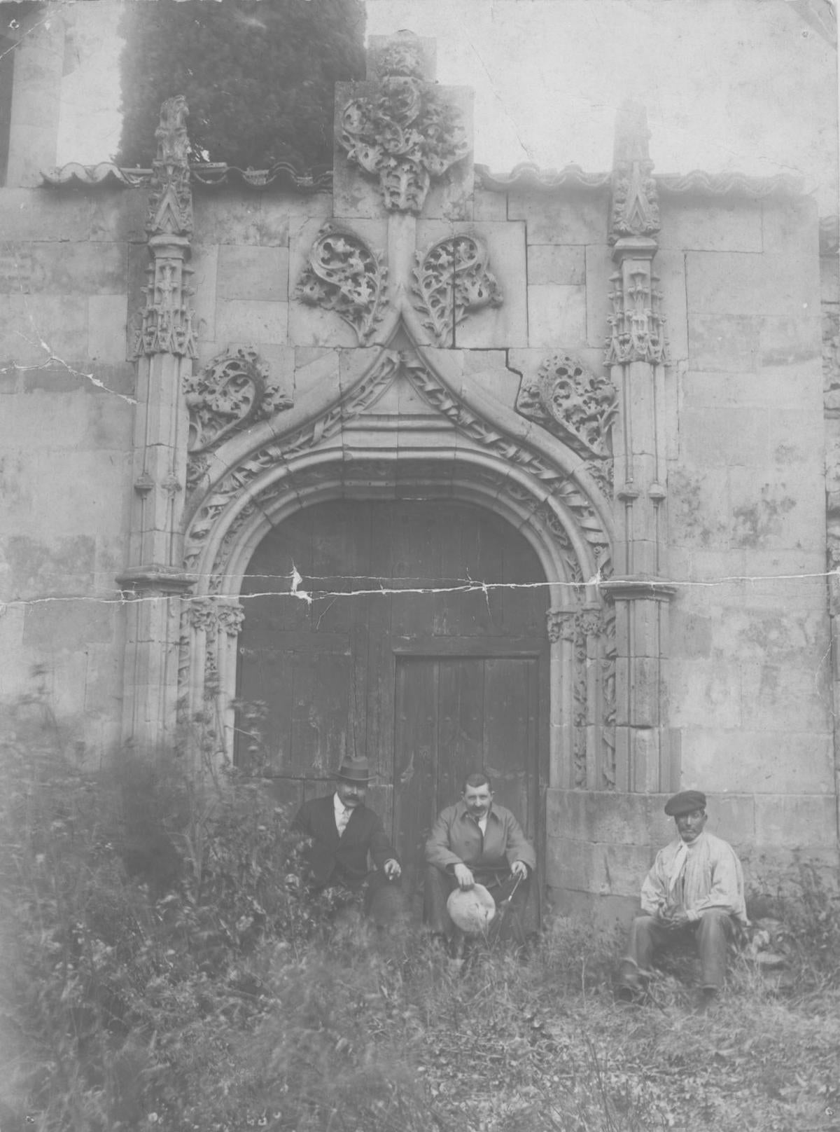 Foto inédita de tres personas posando ante la portada gótica de San Adrián en su emplazamiento temporal del antiguo Hospital de la Santísima Trinidad | ARCHIVO MIQUEL UTRILLO (núm. inv. 3.442-9). © ARCHIVO FOTOGRÁFICO DEL CONSORCI DE PATRIMONI DE SITGES