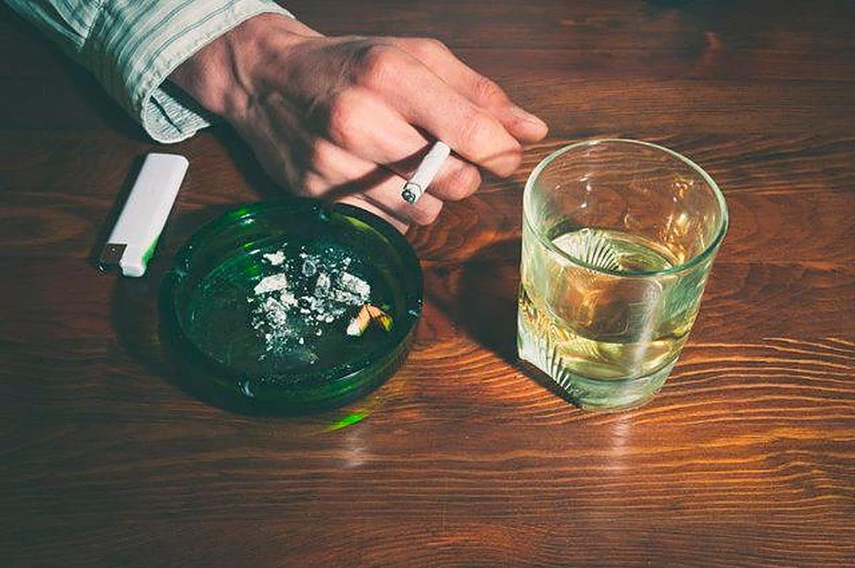 Una personas con un cigarro y una copa de alcohol.