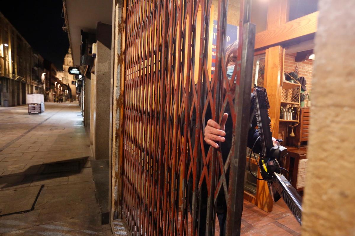 Un hostelero cerrando la trapa de su bar en Salamanca.