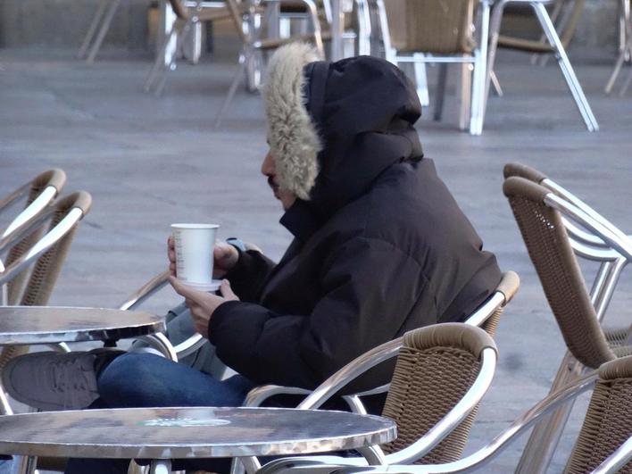 Un ciudadano tomando ayer, bien abrigado, un café en una terraza.