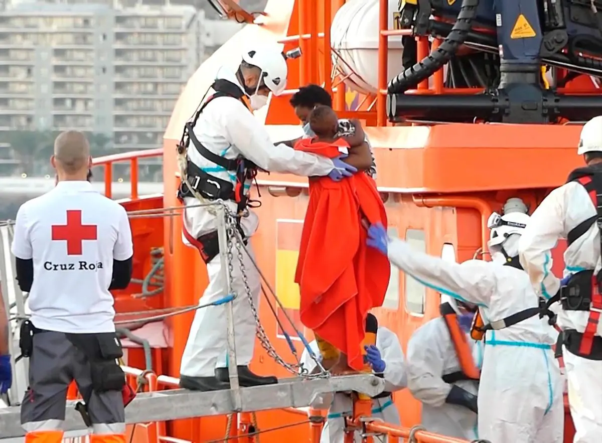 Un miembro de la Cruz Roja ayuda a bajar del barco a una mujer migrante con su niño en el puerto de Arguineguín