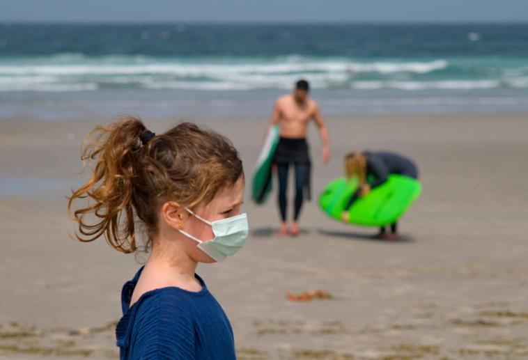 Una niña con la mascarilla en la playa.