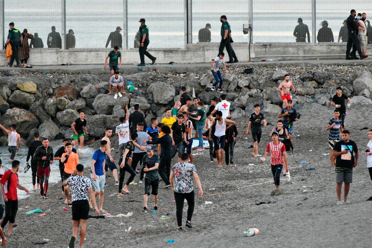 Personas migrantes caminan por la playa del Tarajal.