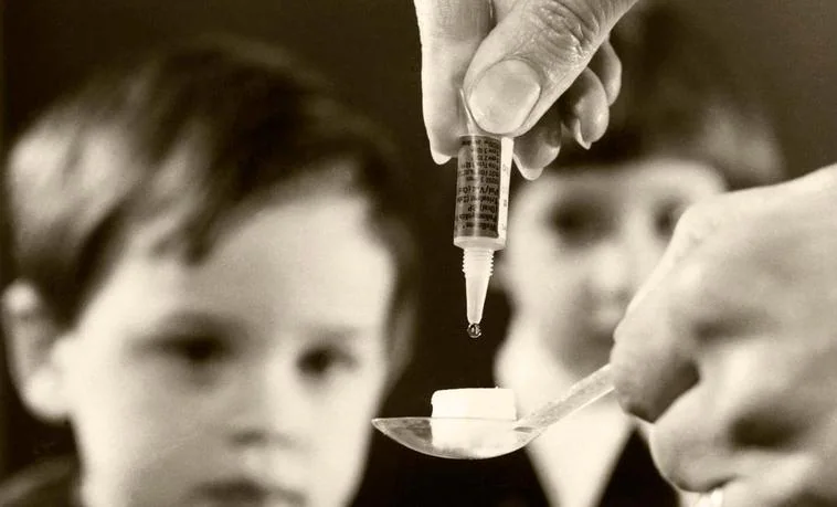Un sanitario empapa un terrón de azúcar con la antigua vacuna de la polio ante la mirada del niño que la iba a tomar.