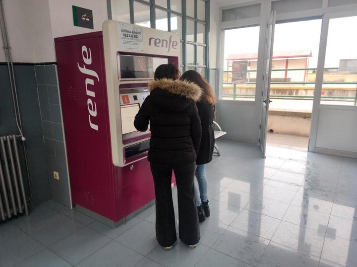 Dos jóvenes sacando un billete de tren en la máquina automática de la estación.