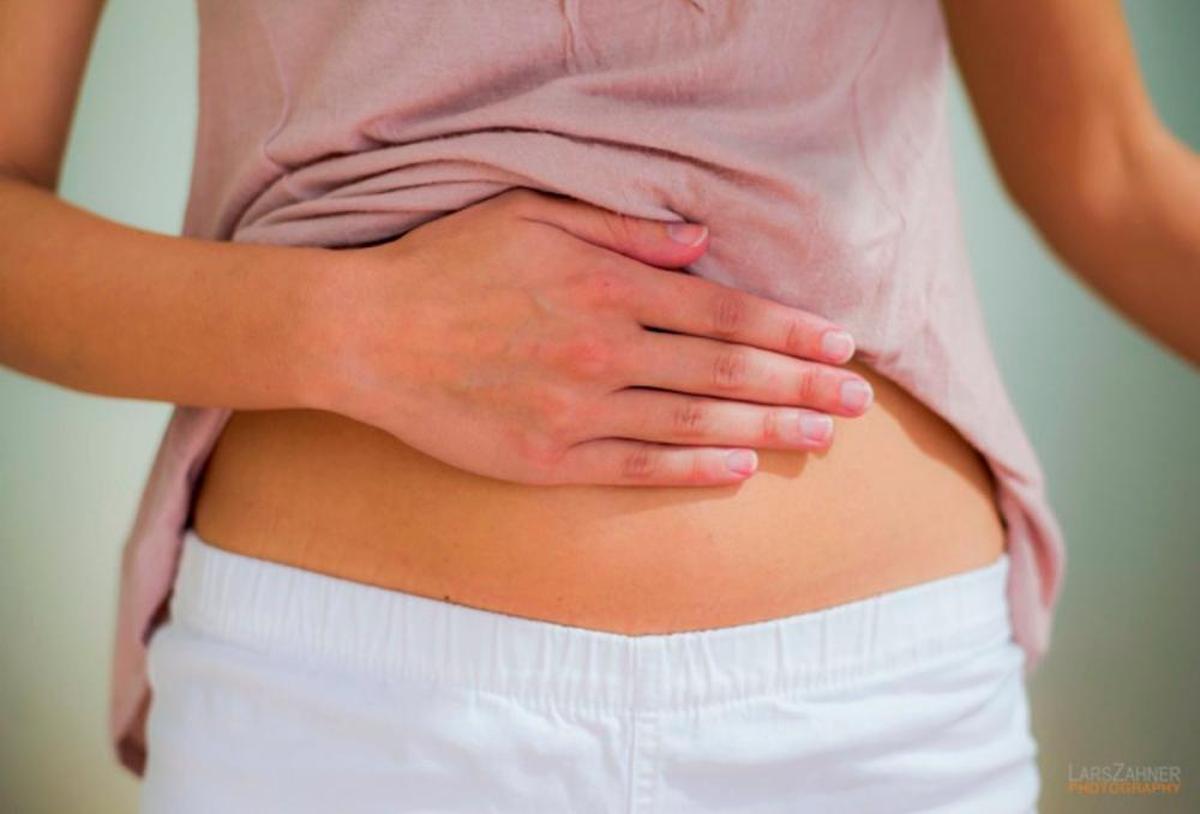 Una mujer apoya su mano sobre el abdomen.