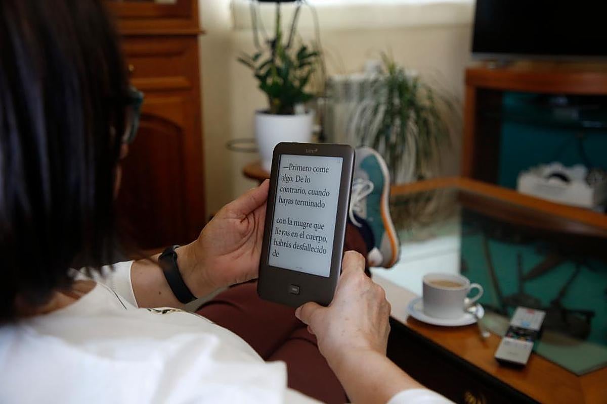 Una mujer, con su lectura digital en el salón de su casa.