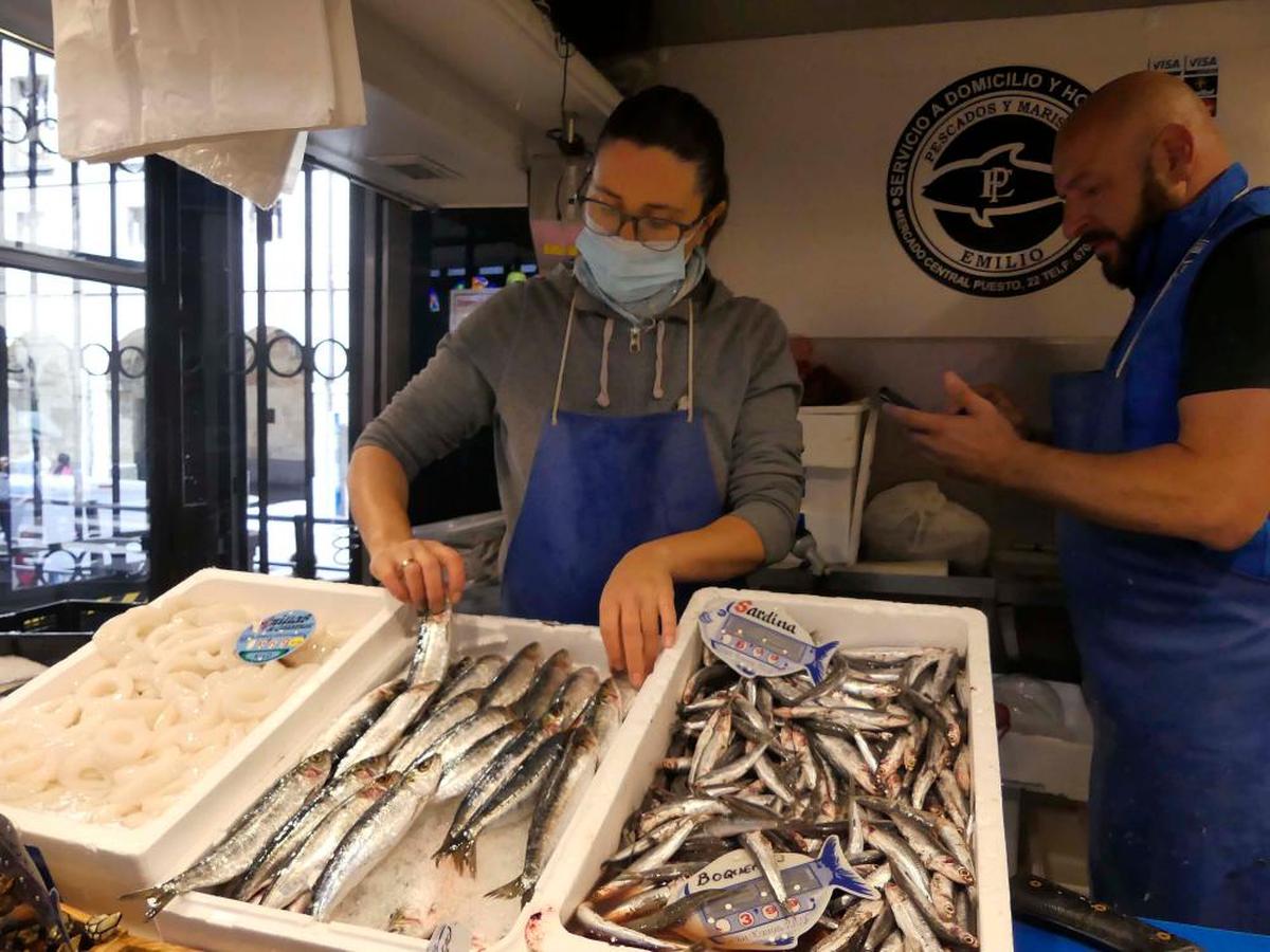 Una dependienta coloca una caja de sardinas en una pescadería del Mercado