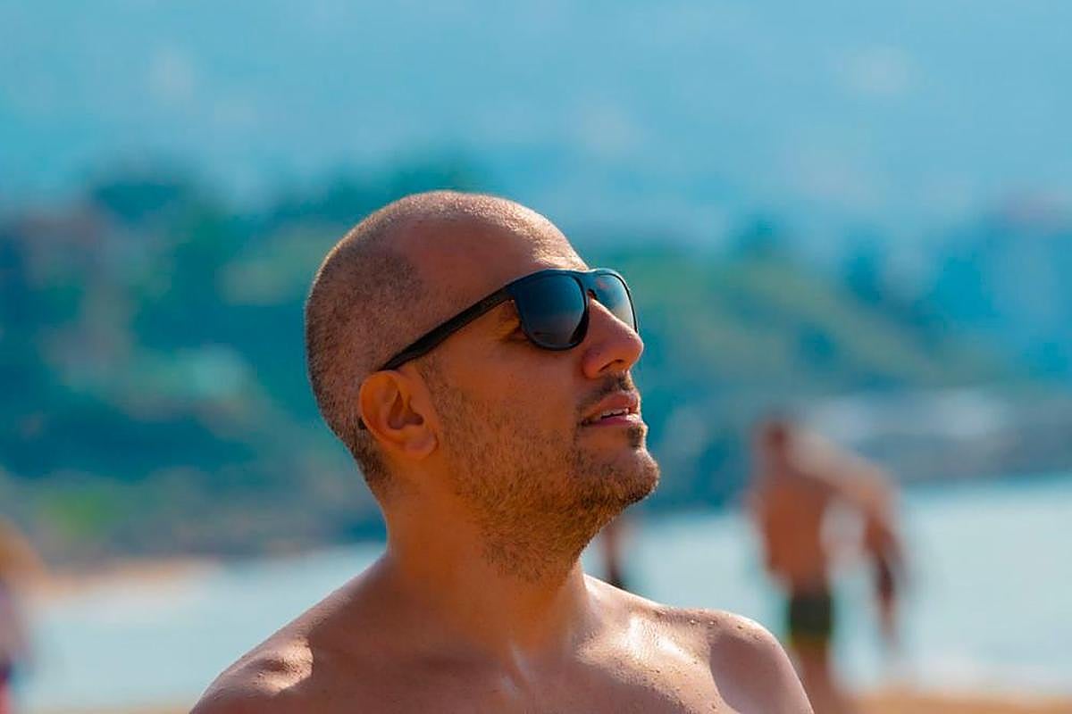 Un hombre posa con gafas en la playa.
