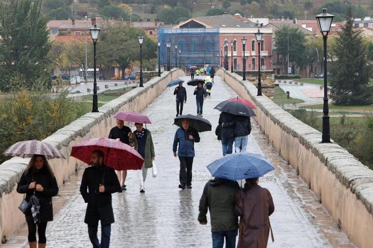 Varios peatones cruzan el Puente Romano lloviendo