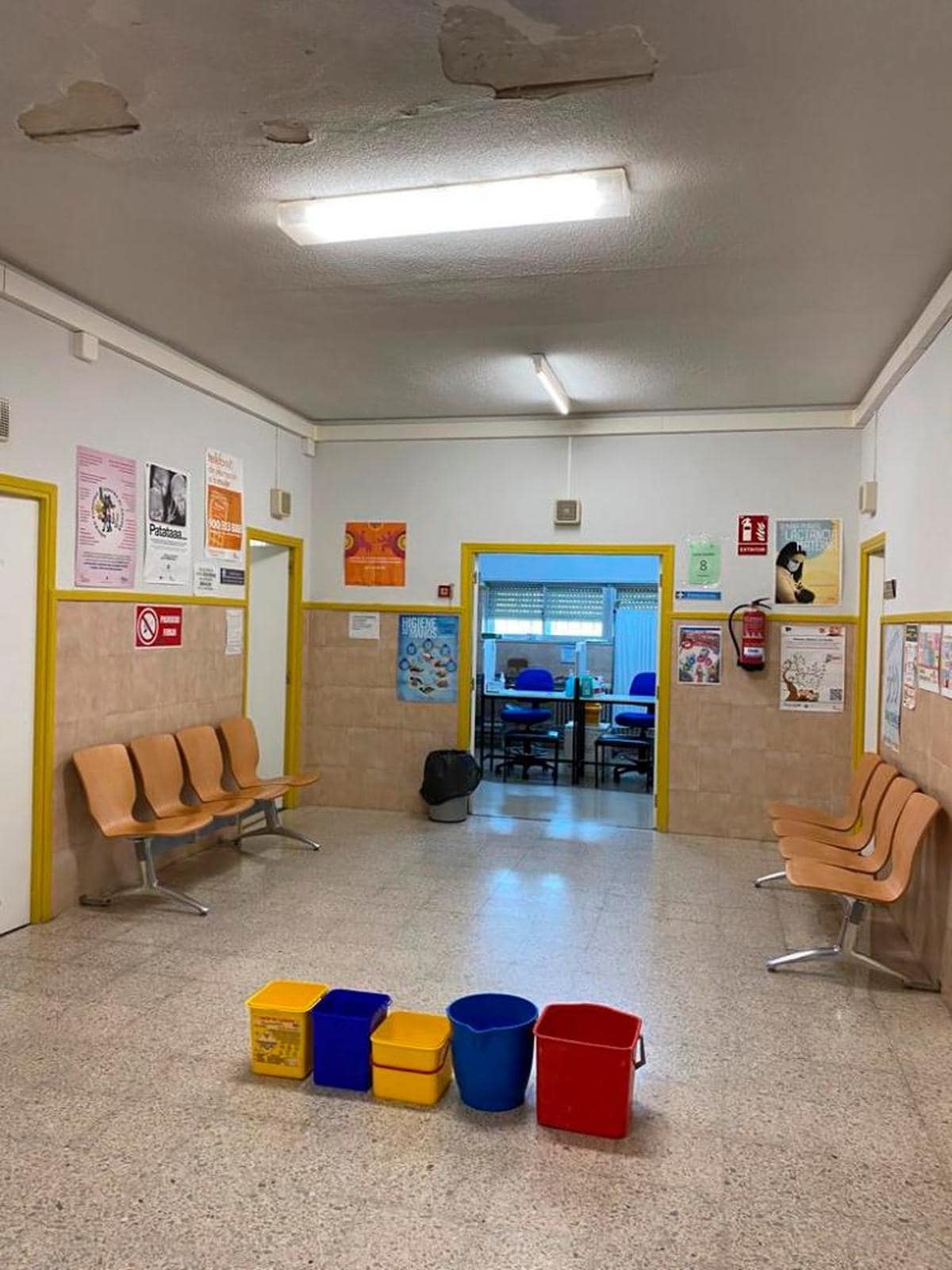 Sala de espera del centro de salud con cubos por la entrada de agua