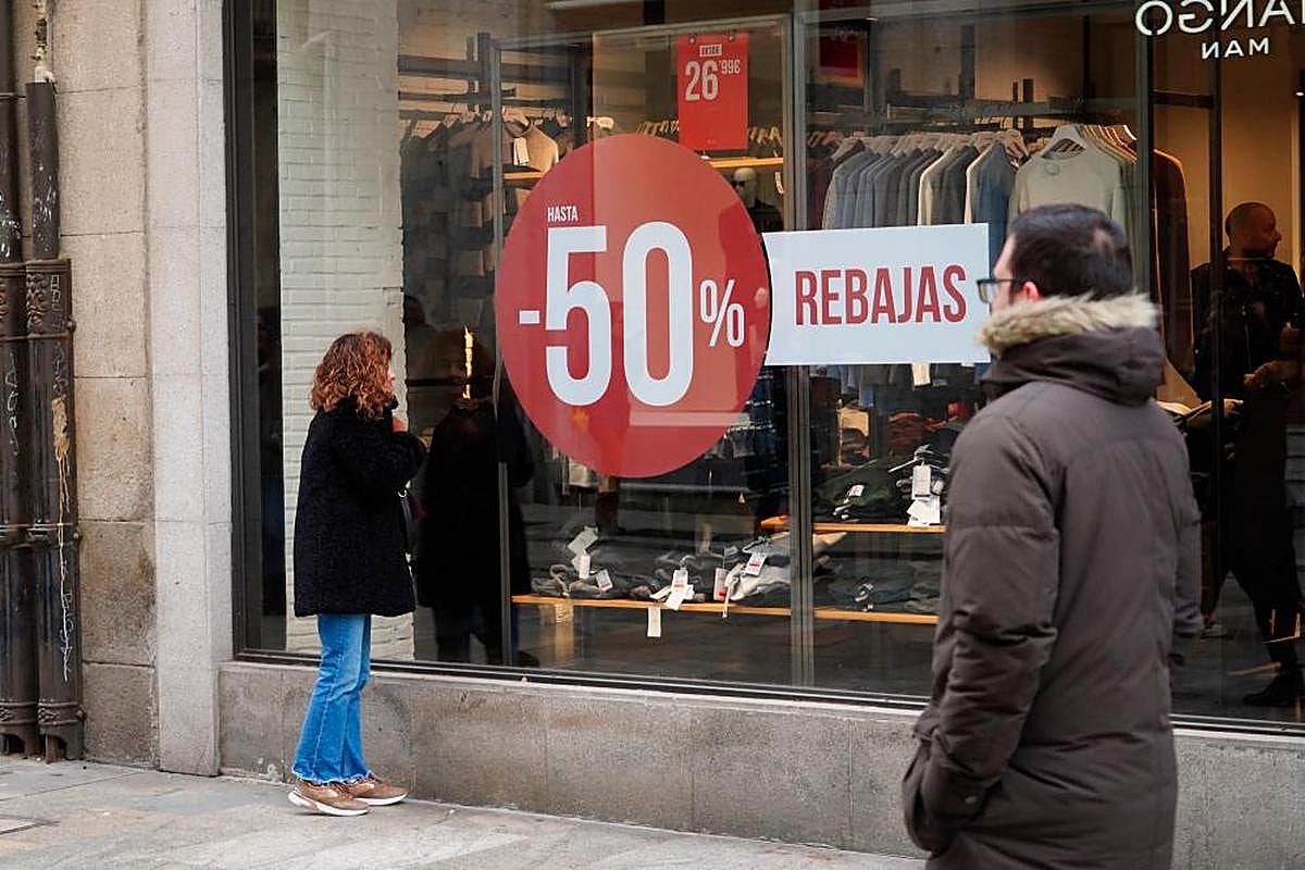 Una mujer mira el escaparate de una tienda de ropa con el anuncio de rebajas de hasta el 50%.