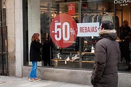 Una mujer mira el escaparate de una tienda de ropa con el anuncio de rebajas de hasta el 50%.