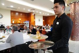 Camarero sirviendo en un restaurante lleno de comensales. LAYA