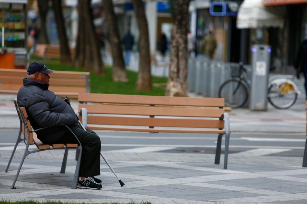 Un hombre mayor descansa en medio de unos bancos completamente vacíos