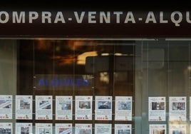 Una persona mirando carteles de viviendas en el escaparate de una inmobiliaria.