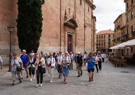 Un grupo de viajeros extranjeros encabezados por una guía turística pasan junto a la iglesia de La Clerecía.