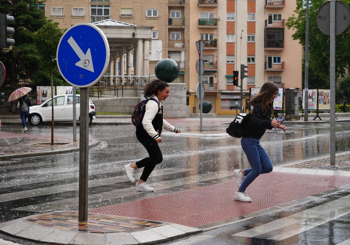 Jóvenes salmantinas cruzan un paso de peatones bajo la lluvia.